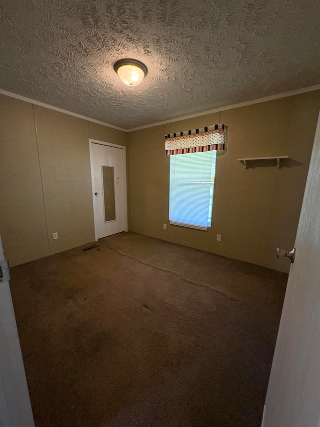 empty room featuring a textured ceiling, ornamental molding, and carpet floors