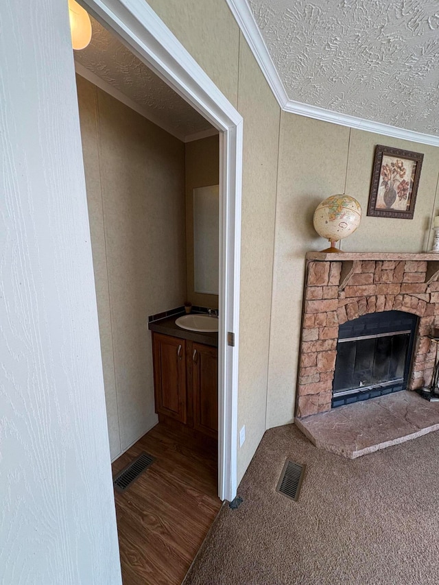 interior space featuring sink, a textured ceiling, a fireplace, wood-type flooring, and crown molding