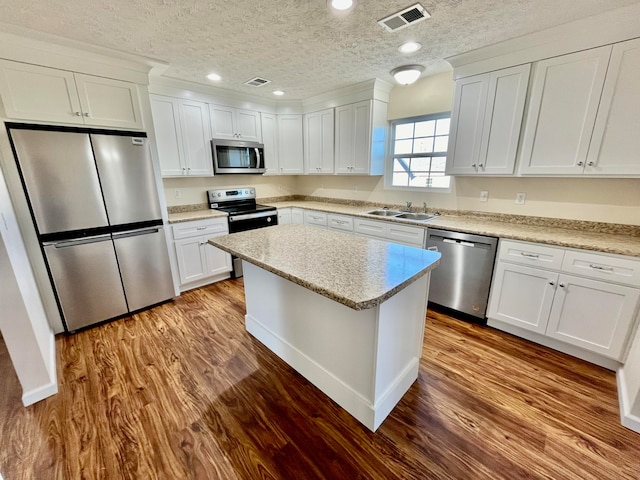 kitchen with a textured ceiling, sink, white cabinetry, light wood-type flooring, and appliances with stainless steel finishes