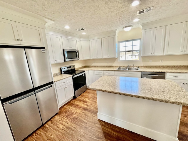 kitchen with a center island, appliances with stainless steel finishes, sink, white cabinets, and light hardwood / wood-style flooring