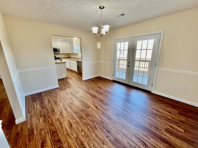 unfurnished dining area with dark wood-type flooring, an inviting chandelier, french doors, and a textured ceiling