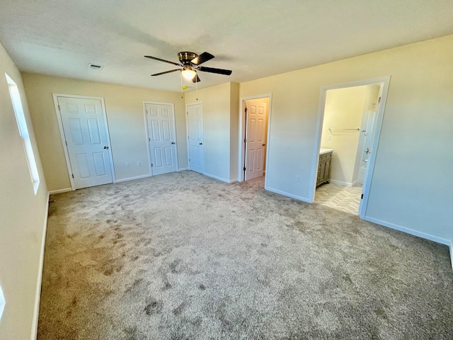 unfurnished bedroom with light carpet, two closets, ceiling fan, and ensuite bathroom