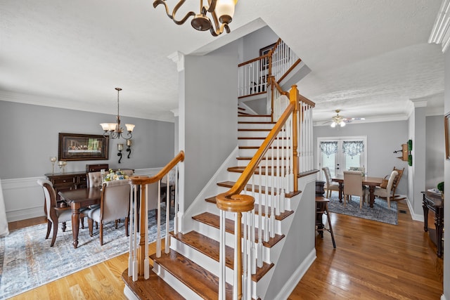 stairway featuring a textured ceiling, hardwood / wood-style floors, ornamental molding, and a chandelier