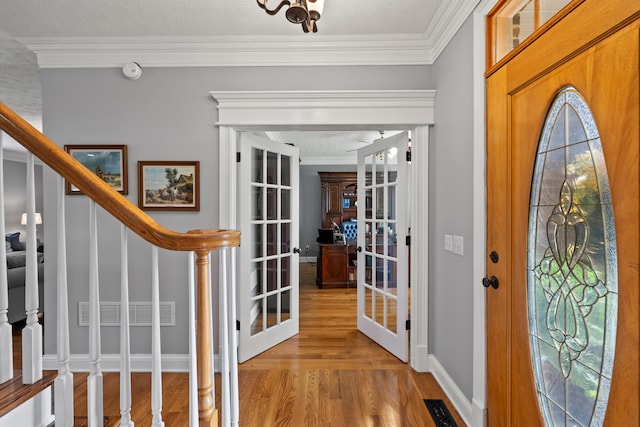 foyer entrance with ornamental molding, french doors, light hardwood / wood-style flooring, and a textured ceiling