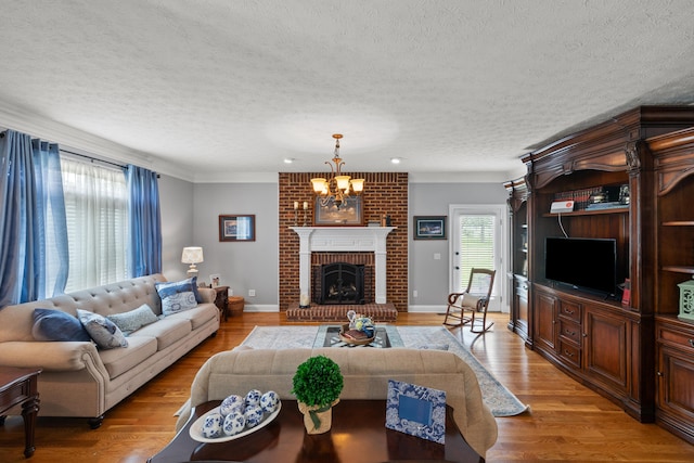 living room featuring a notable chandelier, a textured ceiling, ornamental molding, a fireplace, and light hardwood / wood-style flooring