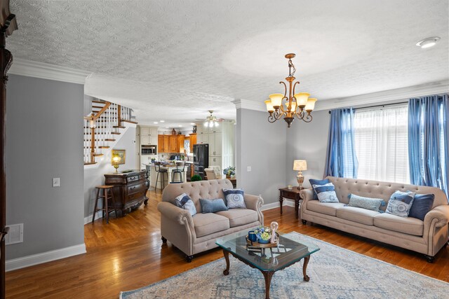 living room with ornamental molding, ceiling fan with notable chandelier, wood-type flooring, and a textured ceiling