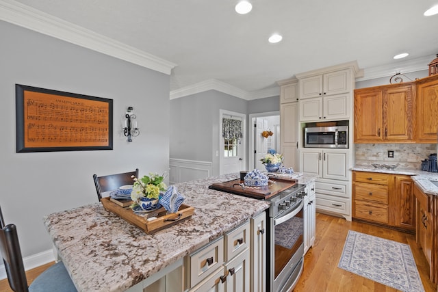 kitchen with a center island, light hardwood / wood-style flooring, ornamental molding, light stone countertops, and appliances with stainless steel finishes