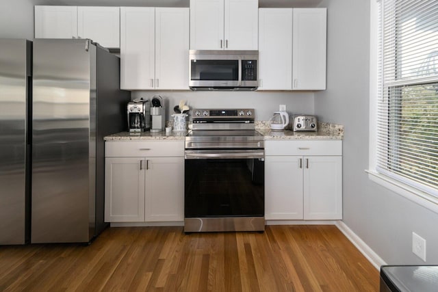 kitchen featuring light stone countertops, appliances with stainless steel finishes, dark hardwood / wood-style flooring, and white cabinetry