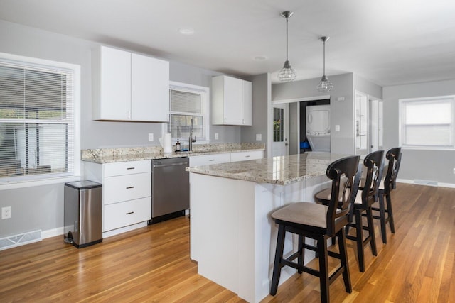 kitchen with white cabinetry, a center island, stainless steel dishwasher, pendant lighting, and light hardwood / wood-style floors