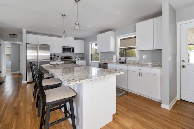 kitchen featuring white cabinets, decorative light fixtures, a center island, and appliances with stainless steel finishes