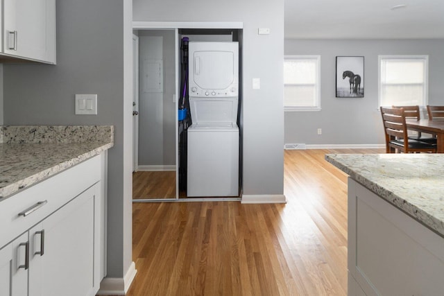 kitchen featuring light stone countertops, stacked washer and dryer, white cabinetry, and light hardwood / wood-style floors