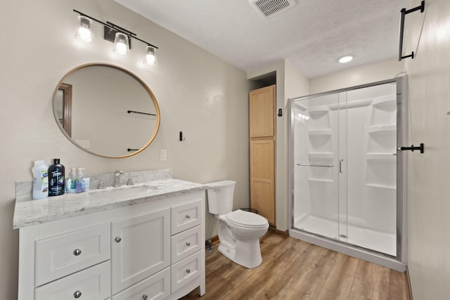 bathroom featuring a textured ceiling, toilet, vanity, a shower with shower door, and hardwood / wood-style flooring