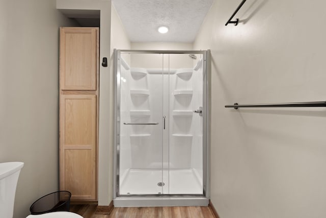 bathroom with a shower with shower door, toilet, wood-type flooring, and a textured ceiling