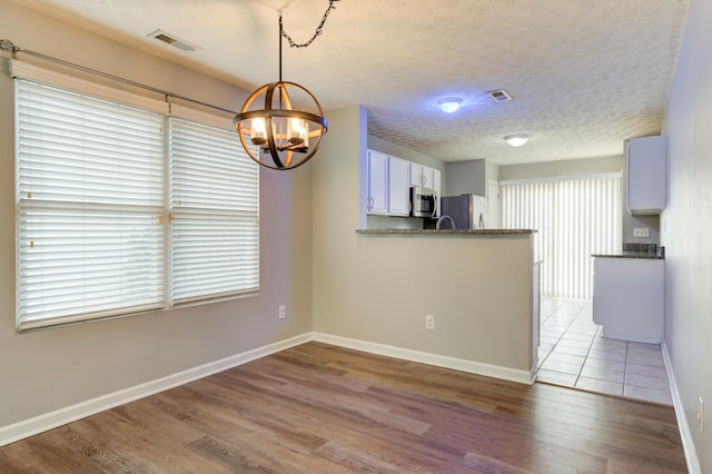 interior space with a textured ceiling, light wood-type flooring, and a notable chandelier