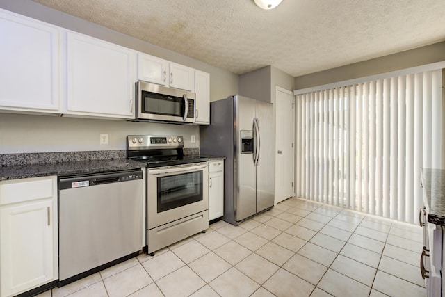 kitchen featuring dark stone counters, a textured ceiling, stainless steel appliances, light tile patterned floors, and white cabinets