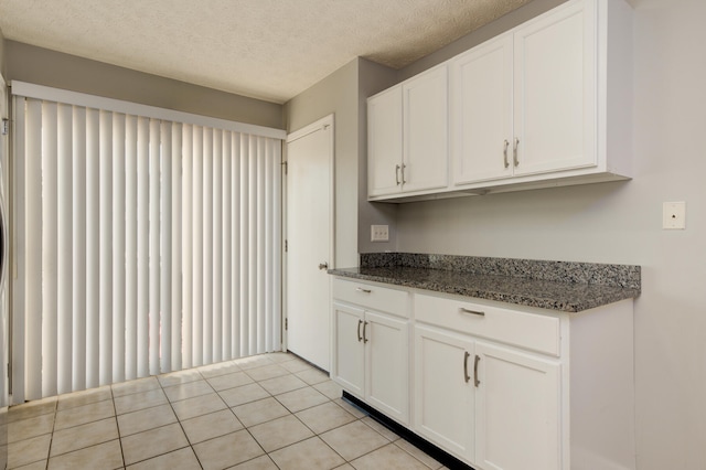 kitchen with dark stone countertops, white cabinetry, a textured ceiling, and light tile patterned floors