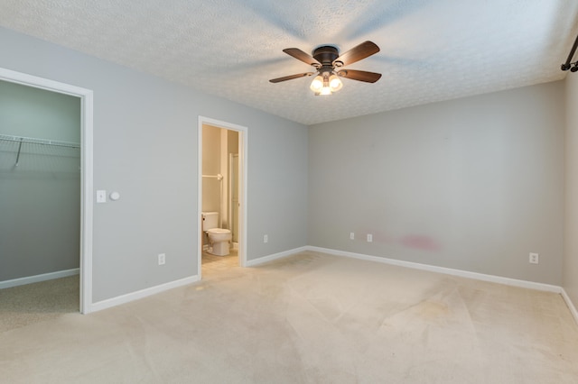 unfurnished bedroom with ceiling fan, a walk in closet, a textured ceiling, and ensuite bath