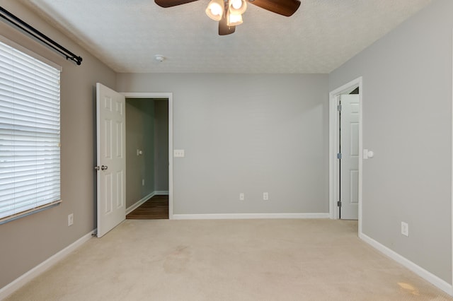 empty room featuring light carpet, a wealth of natural light, a textured ceiling, and ceiling fan