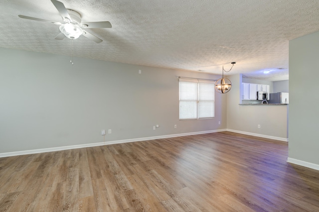 empty room with ceiling fan with notable chandelier, light hardwood / wood-style floors, and a textured ceiling