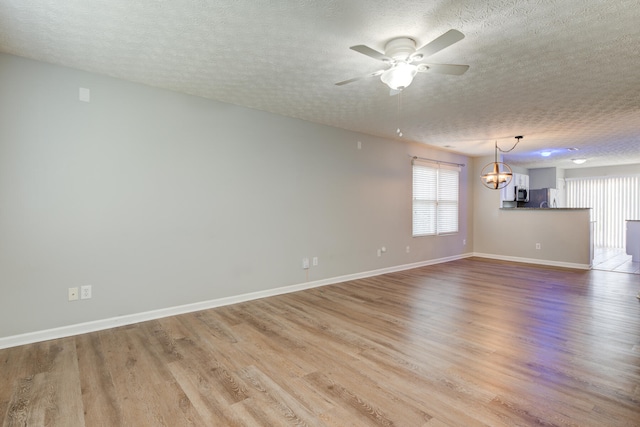 unfurnished living room featuring ceiling fan with notable chandelier, light hardwood / wood-style floors, and a textured ceiling