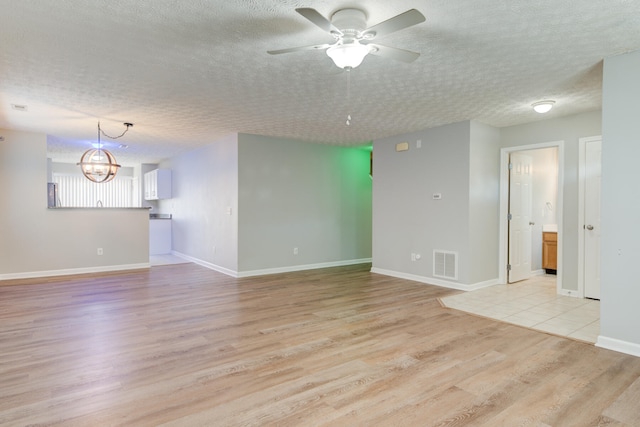 spare room featuring ceiling fan with notable chandelier, light hardwood / wood-style floors, and a textured ceiling