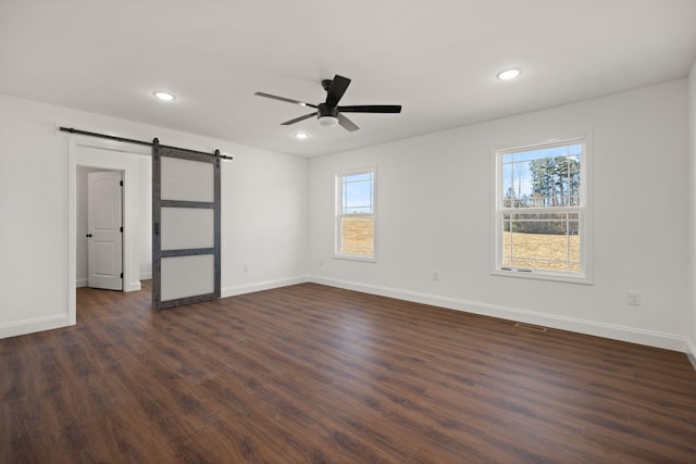 unfurnished bedroom with ceiling fan, a barn door, and dark hardwood / wood-style floors