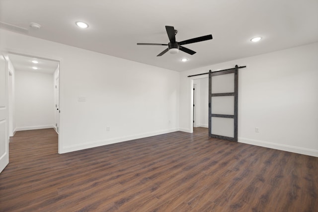 empty room featuring ceiling fan, a barn door, and dark wood-type flooring