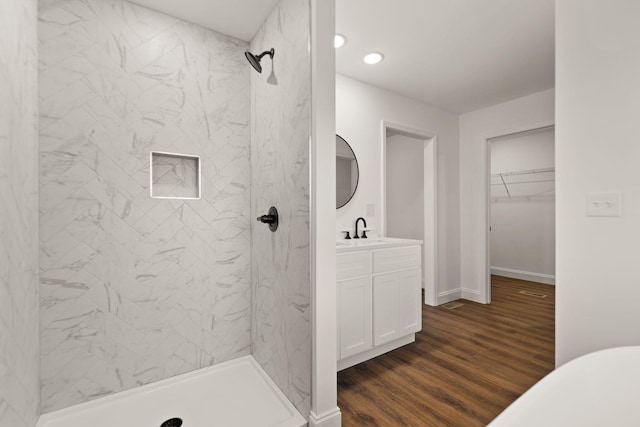 bathroom with hardwood / wood-style flooring, vanity, and tiled shower