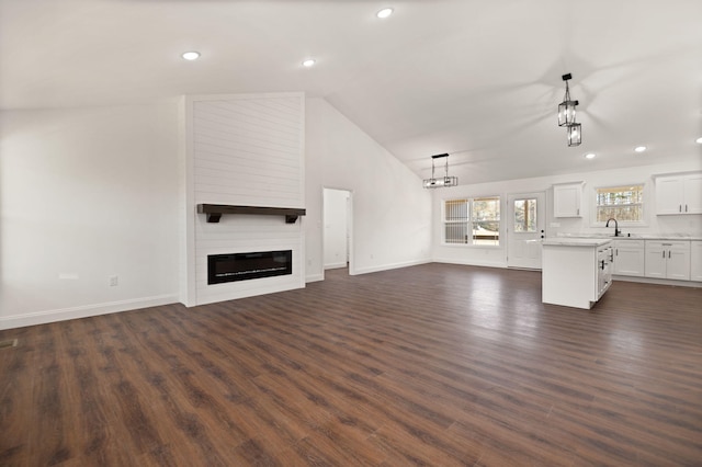 unfurnished living room featuring a large fireplace, high vaulted ceiling, dark wood-type flooring, and sink