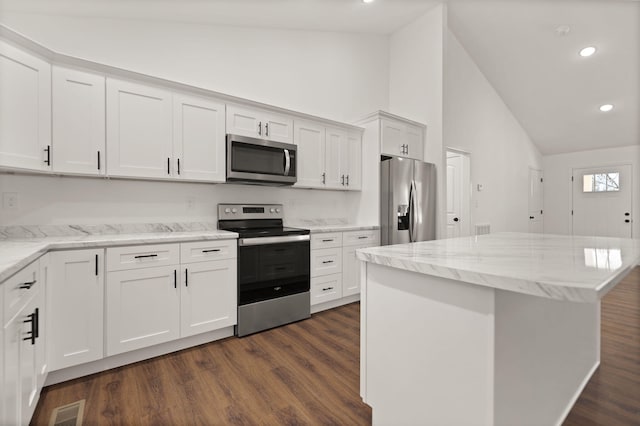 kitchen with white cabinets, dark hardwood / wood-style floors, light stone countertops, appliances with stainless steel finishes, and a kitchen island