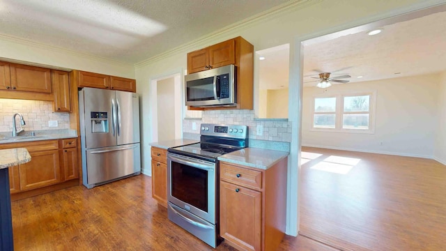 kitchen with appliances with stainless steel finishes, hardwood / wood-style floors, tasteful backsplash, sink, and ornamental molding