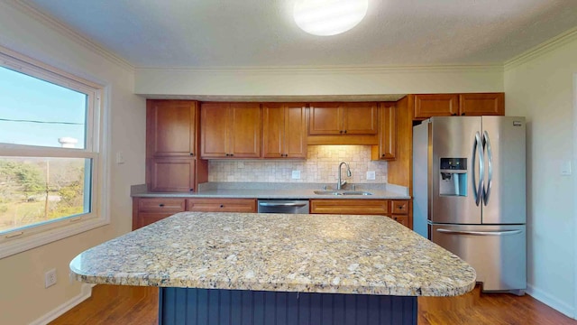 kitchen with sink, hardwood / wood-style flooring, appliances with stainless steel finishes, a kitchen island, and decorative backsplash