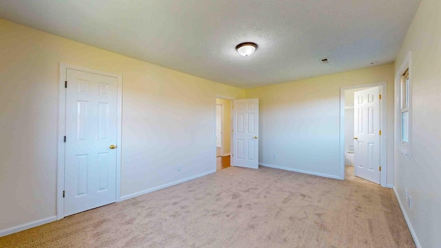 unfurnished bedroom featuring light colored carpet, ensuite bathroom, and a textured ceiling