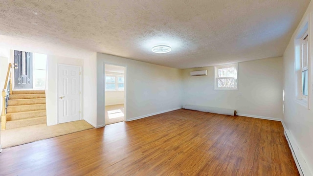 spare room featuring a wall mounted air conditioner, a textured ceiling, wood-type flooring, and a baseboard heating unit