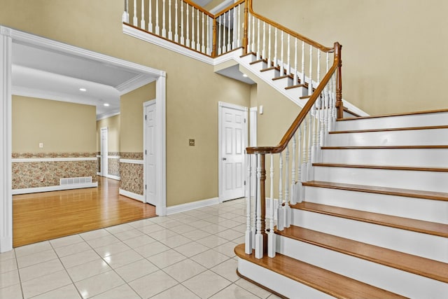 stairway with a towering ceiling, ornamental molding, and tile patterned flooring