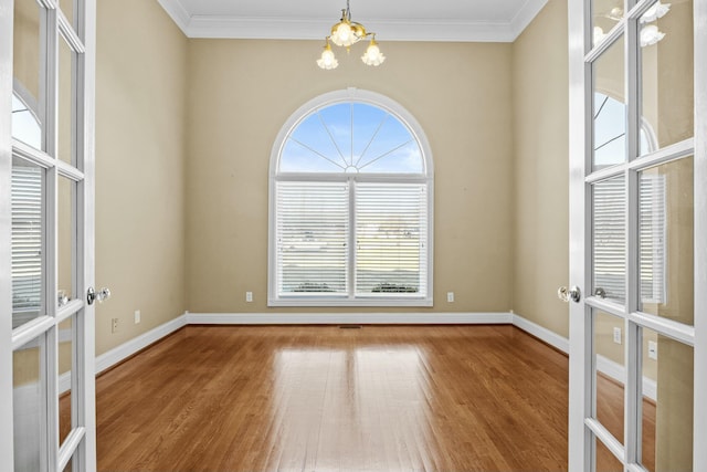 unfurnished room featuring an inviting chandelier, wood-type flooring, ornamental molding, and french doors