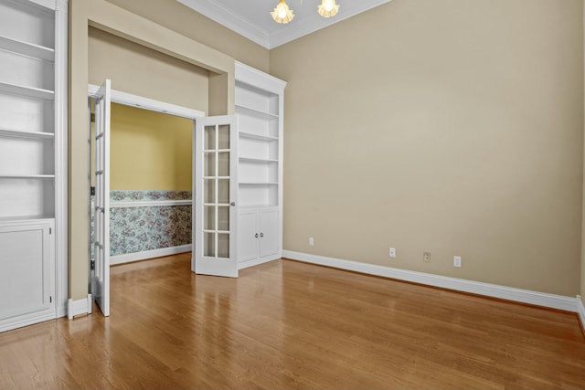 empty room featuring crown molding, a notable chandelier, hardwood / wood-style flooring, and built in shelves