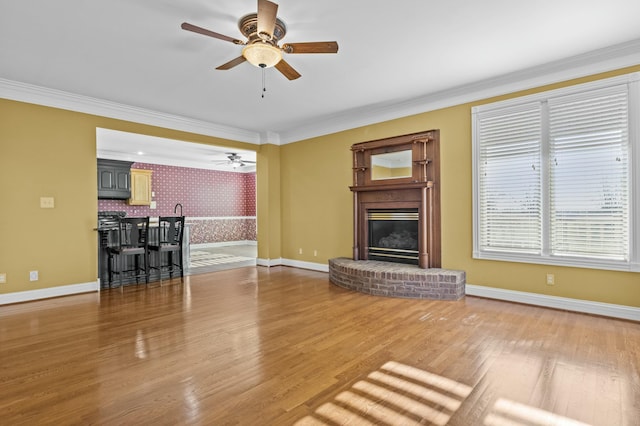 unfurnished living room featuring a brick fireplace, wood-type flooring, ornamental molding, and ceiling fan