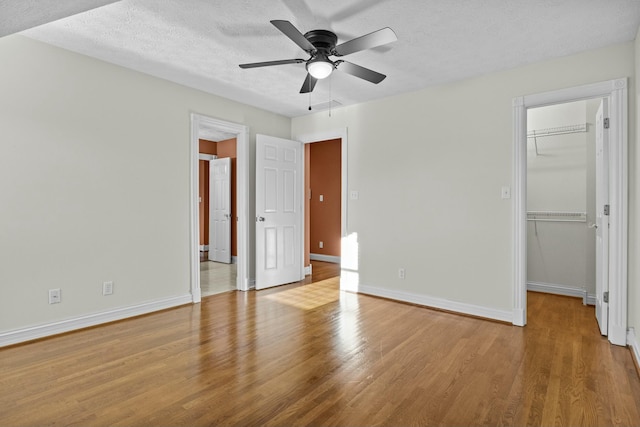 unfurnished bedroom featuring light hardwood / wood-style flooring, a spacious closet, ceiling fan, a textured ceiling, and a closet