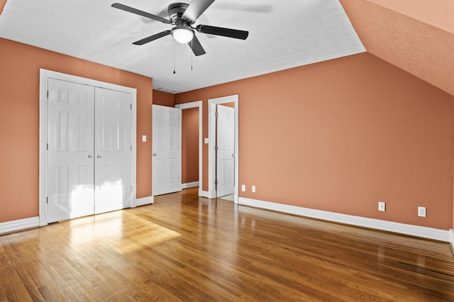 unfurnished bedroom with vaulted ceiling, a textured ceiling, a closet, ceiling fan, and hardwood / wood-style floors