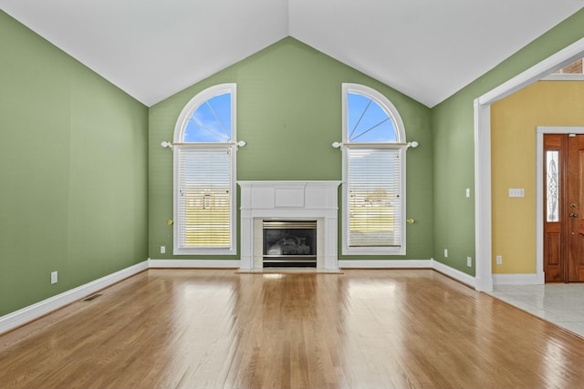 unfurnished living room featuring high vaulted ceiling, a glass covered fireplace, wood finished floors, and baseboards