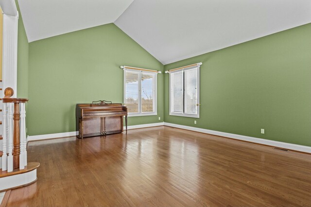 empty room with baseboards, wood finished floors, visible vents, and high vaulted ceiling