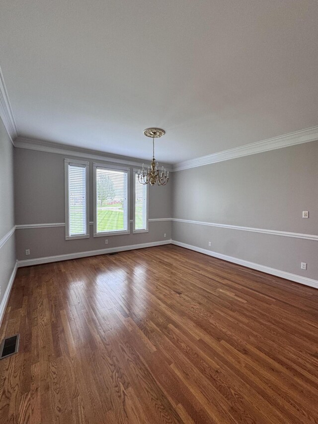 spare room with visible vents, a chandelier, ornamental molding, and dark wood-style flooring