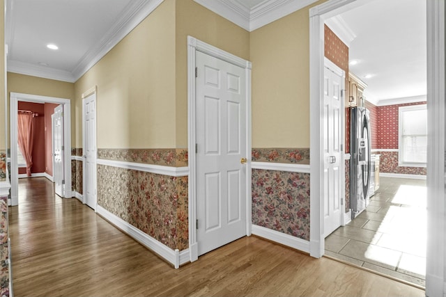 corridor featuring wallpapered walls, baseboards, wood finished floors, and ornamental molding