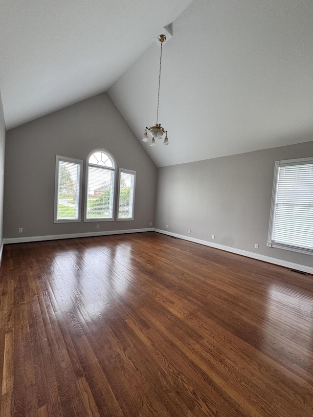 empty room featuring an inviting chandelier, lofted ceiling, dark wood-type flooring, and baseboards