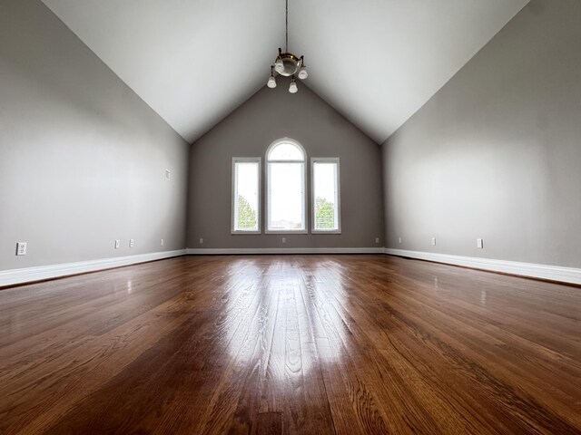 unfurnished living room with baseboards, vaulted ceiling, wood finished floors, and a chandelier