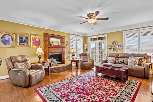 living room with french doors, crown molding, wood-type flooring, a brick fireplace, and ceiling fan