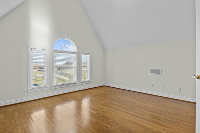 empty room featuring baseboards, wood finished floors, visible vents, and high vaulted ceiling