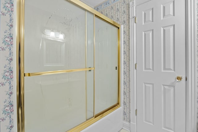 bathroom with wallpapered walls and bath / shower combo with glass door