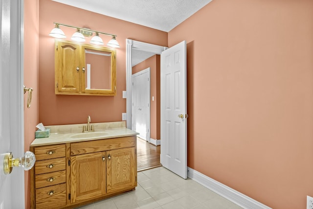 bathroom with a textured ceiling, baseboards, tile patterned flooring, and vanity